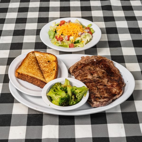 Steak dinner with grilled toast, broccoli, and a side salad on a black and white checkered tablecloth.