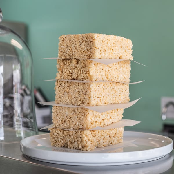 A tall stack of five Rice Krispies treats with parchment paper in between each, on a white plate.