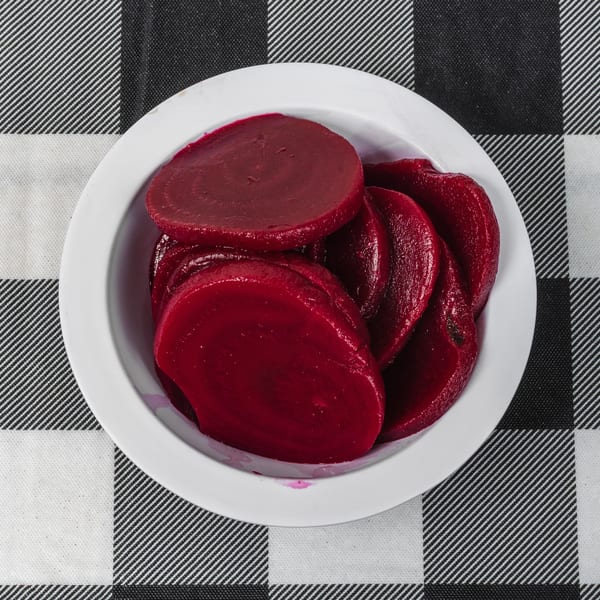 A white bowl filled with sliced, deep red beets sits on a black and white checkered tablecloth.