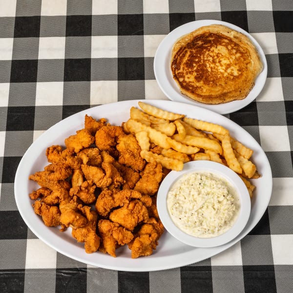 Fried chicken, french fries, coleslaw, and a pancake on a black and white checkered tablecloth.