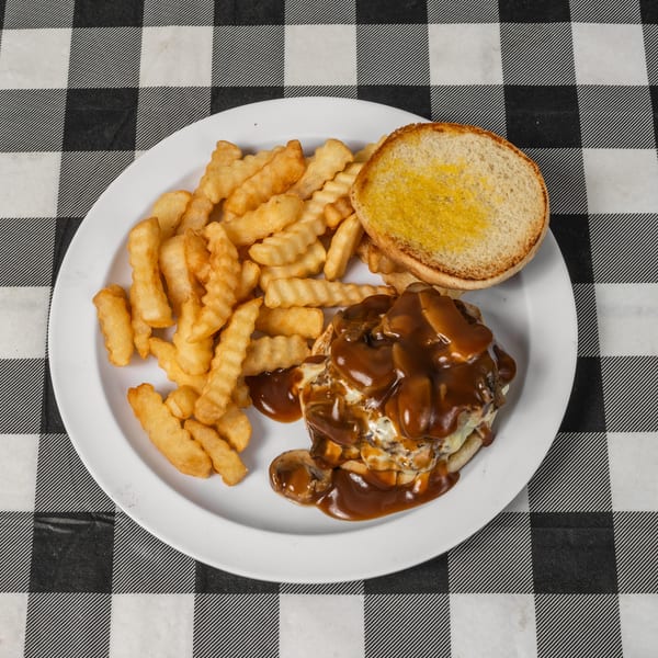 A plate of crinkle-cut fries, a burger patty smothered in gravy, and a toasted bun.