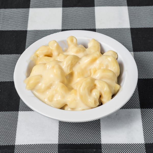 Creamy macaroni and cheese in a white bowl on a black and white checkered tablecloth.