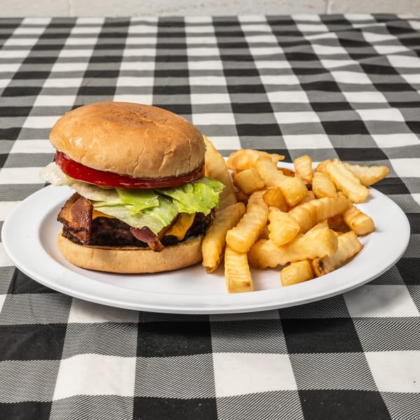 A bacon cheeseburger with lettuce and tomato, served with crinkle-cut fries on a white plate.