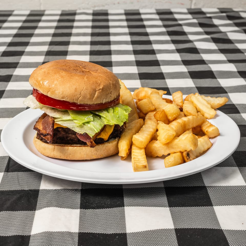 A bacon cheeseburger with lettuce and tomato, served with crinkle-cut fries on a white plate.
