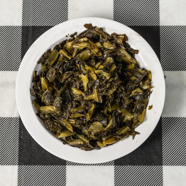 A white plate filled with cooked collard greens, centered on a black and white checkered tablecloth.