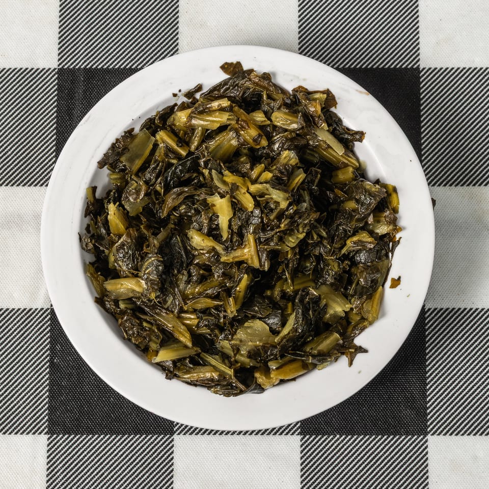A white plate filled with cooked collard greens, centered on a black and white checkered tablecloth.