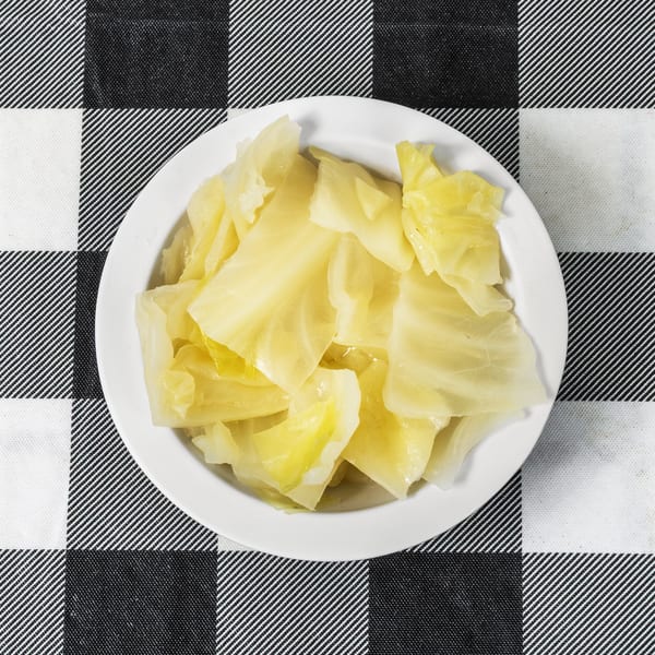 A white bowl filled with steamed cabbage sits on a black and white checkered tablecloth.