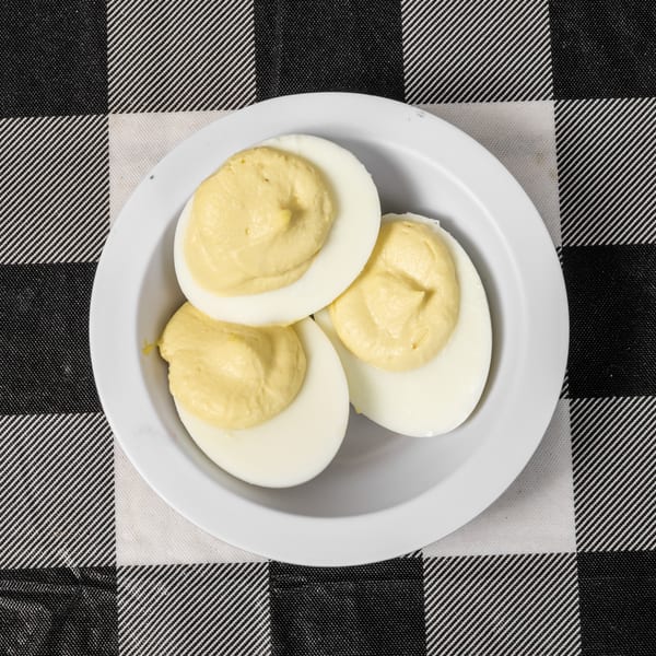 Three deviled egg halves with creamy yellow filling on a white plate, on a black and white checkered tablecloth.