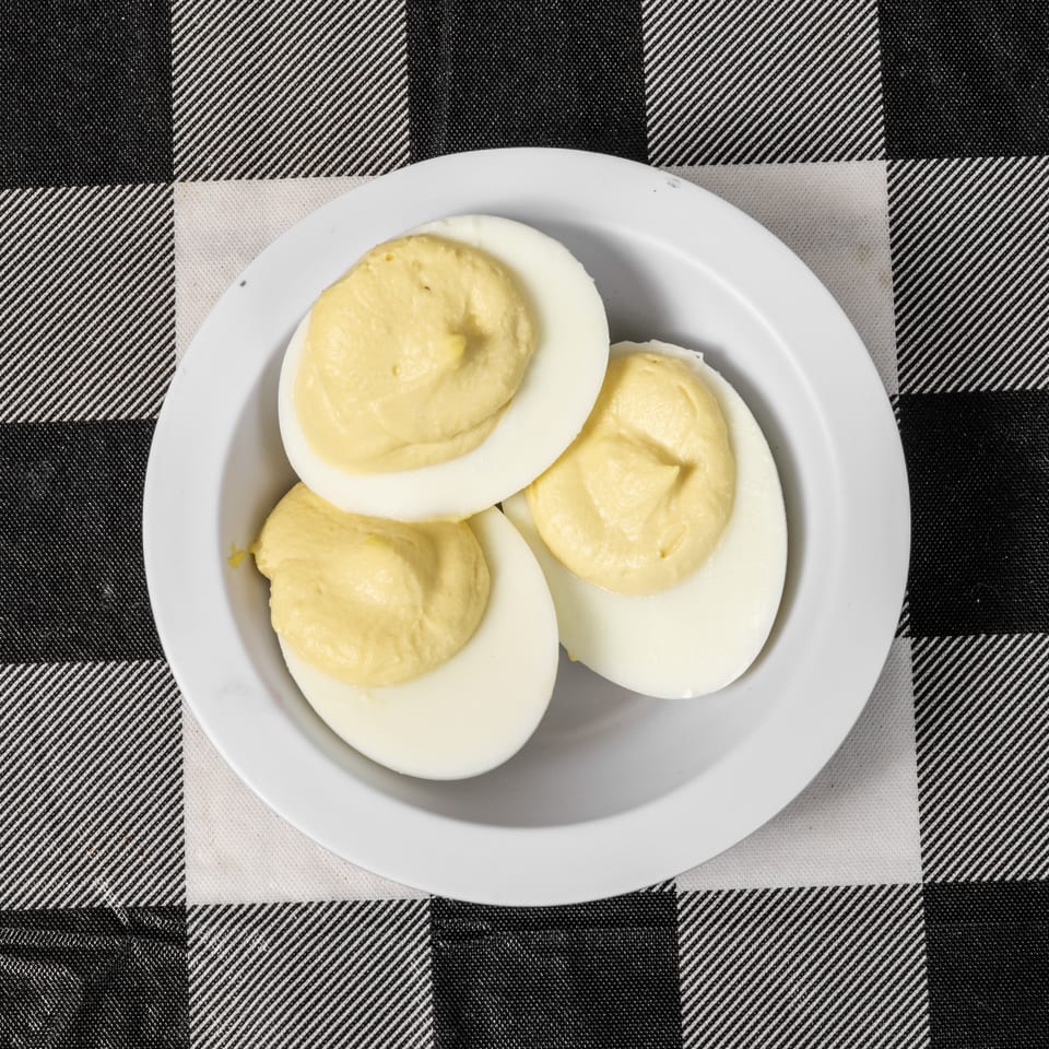 Three deviled egg halves with creamy yellow filling on a white plate, on a black and white checkered tablecloth.