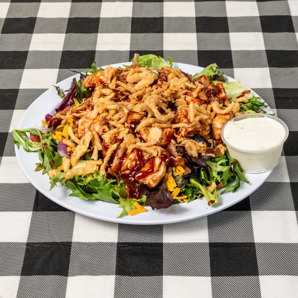 BBQ chicken salad with crispy fried onions, cheese, and ranch dressing on a checkered tablecloth.