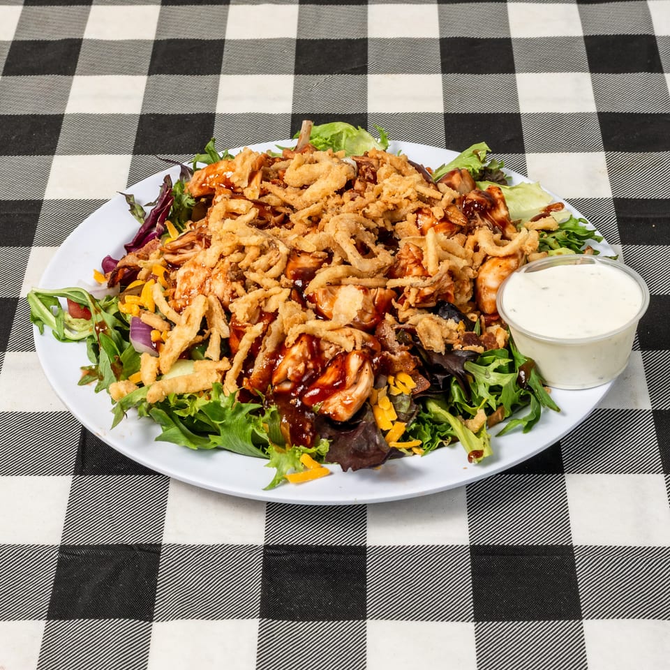 BBQ chicken salad with crispy fried onions, cheese, and ranch dressing on a checkered tablecloth.