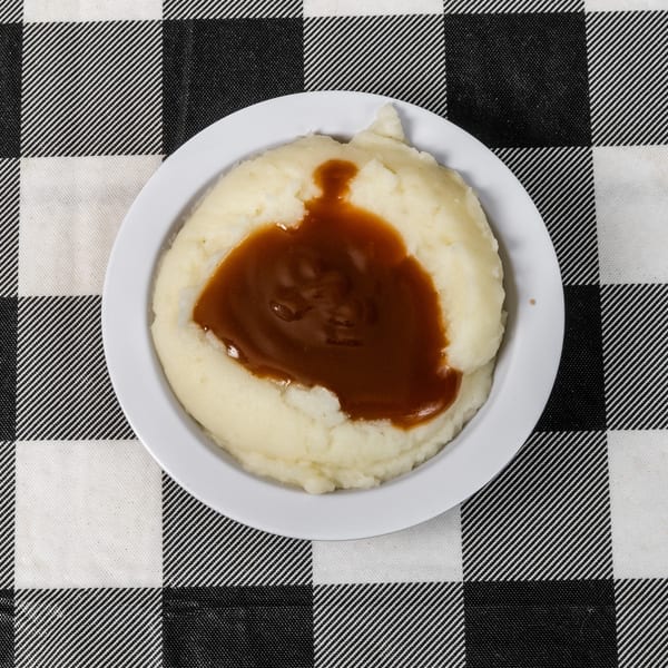 A white bowl of mashed potatoes with brown gravy, on a black and white checkered tablecloth.